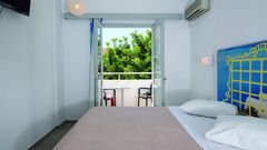 Helles Hotelzimmer mit Doppelbett, Klimaanlage und Zugang zu einem Balkon mit Sitzgelegenheit und Blick ins Grüne – ideal zum Entspannen.