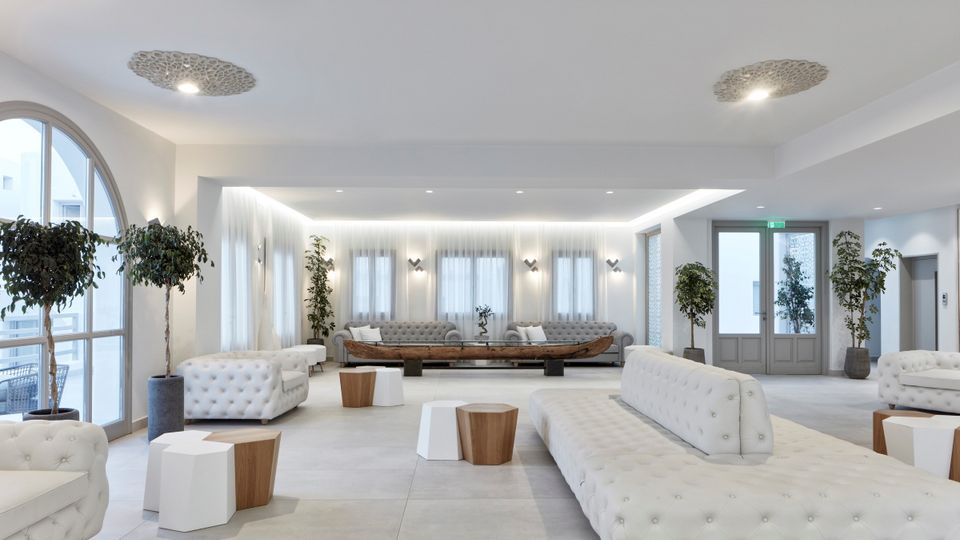 Elegante Hotel-Lobby im Costa Grand Resort & Spa – großzügiger, lichtdurchfluteter Raum mit modernen weißen Sitzmöbeln, stilvollen Deko-Elementen und mediterranen Pflanzen in minimalistischer, luxuriöser Atmosphäre.