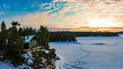 Verschneite Winterhütte über einem vereisten See