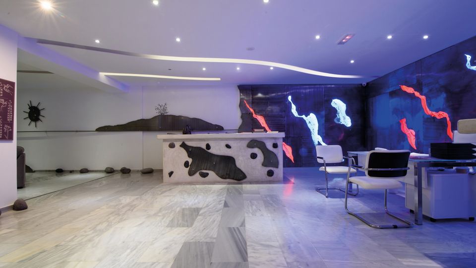 Modern gestalteter Rezeptionsbereich mit kunstvoll beleuchteter Wand in Blau-, Rot- und Weißtönen sowie stilvollen Sitzmöglichkeiten – Empfang mit kreativem Flair.