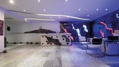 Modern gestalteter Rezeptionsbereich mit kunstvoll beleuchteter Wand in Blau-, Rot- und Weißtönen sowie stilvollen Sitzmöglichkeiten – Empfang mit kreativem Flair.